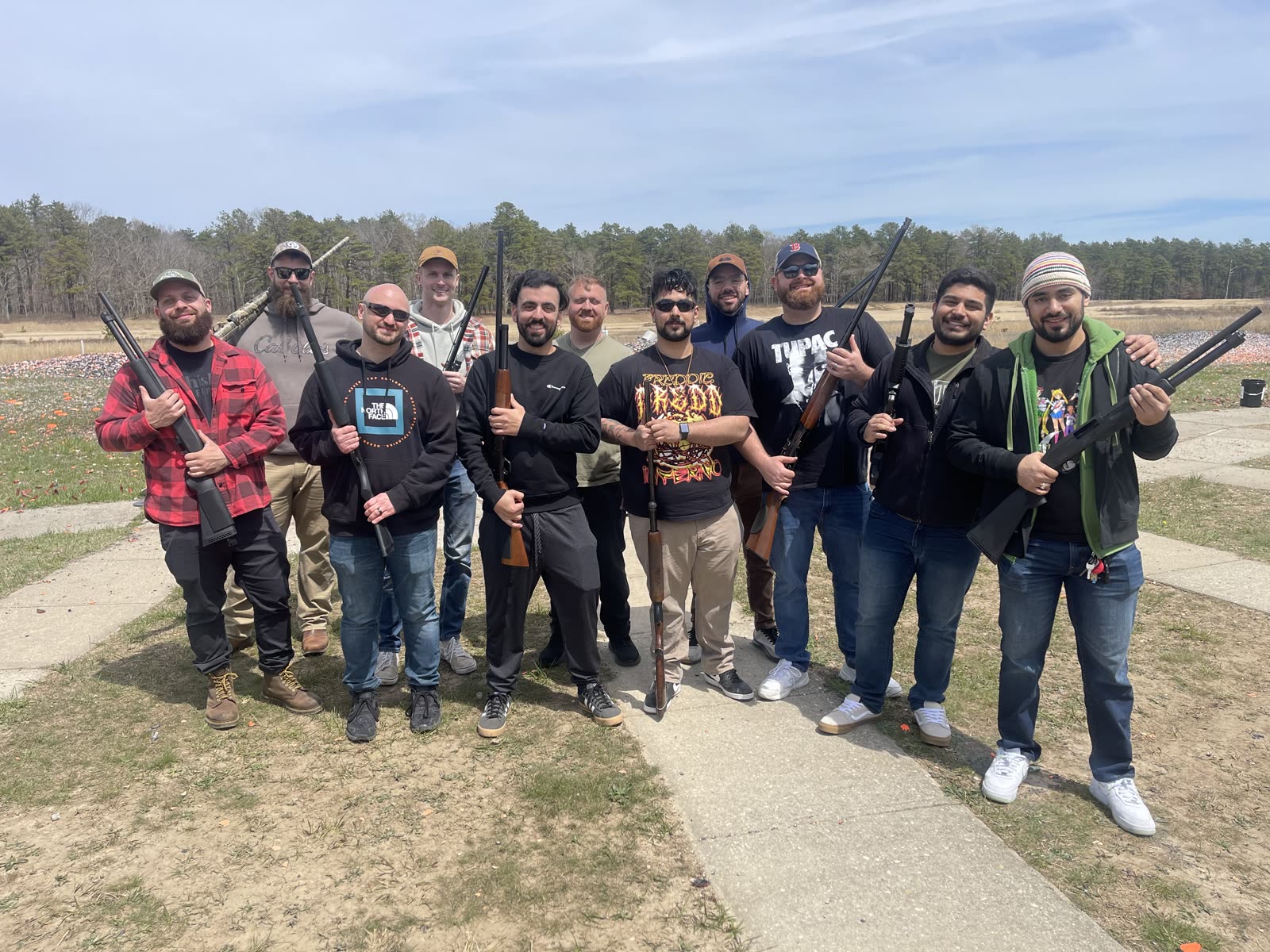 Eleven friends posing with shotguns on an open clay field