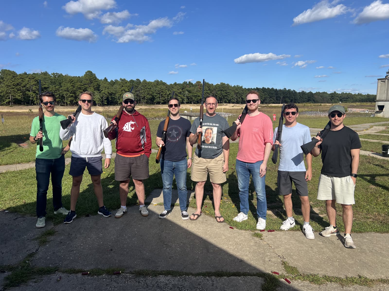 Eight friends in sunglasses posing with shotguns on a bright day