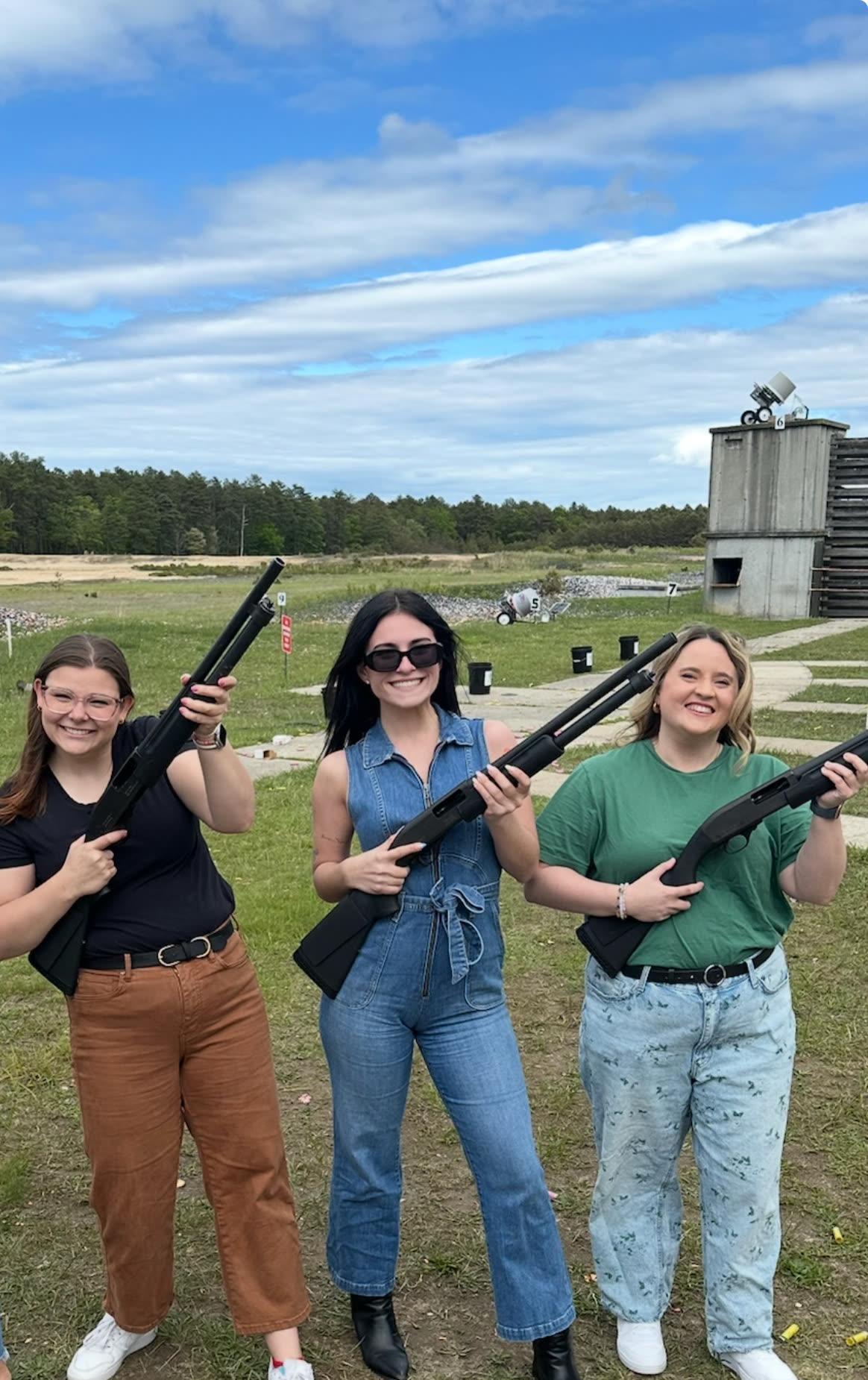 Three friends posing with shotguns on the range, smiling