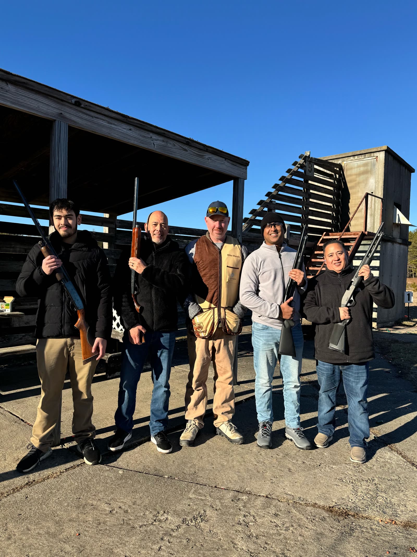 Mike Marelli in a shooting vest with four bird hunters holding shotguns on the range
